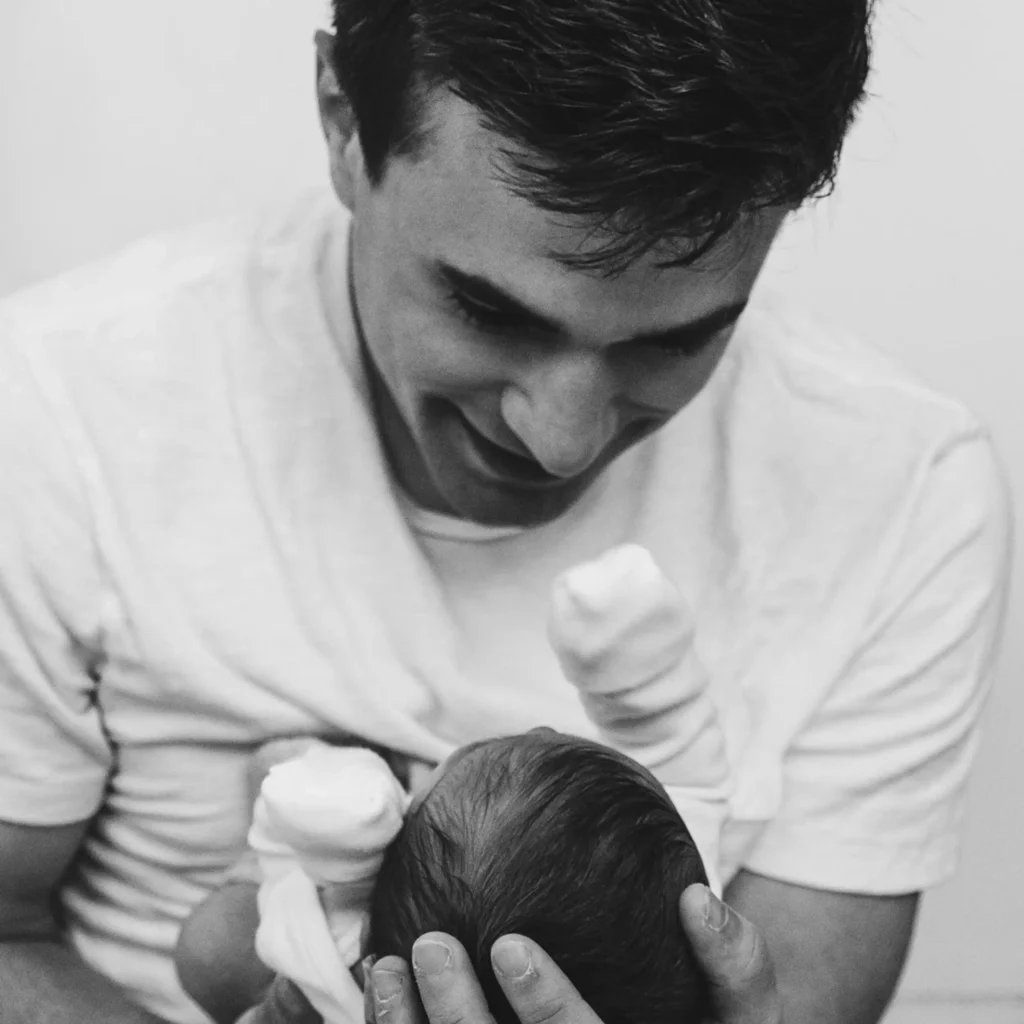 Parent gazes down at newborn baby, smiling and holding them close.