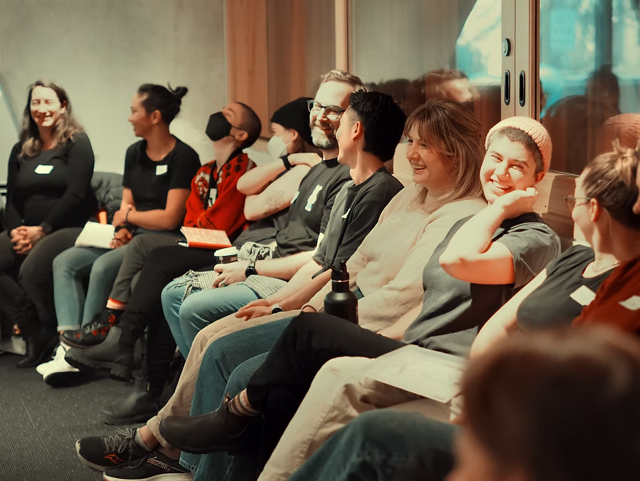 A group of adults sitting in a circle during a workshop, smiling, talking and listening together.