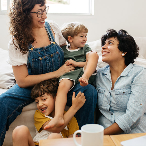 Two parents and two young children smiling and laughing together on a couch at home.