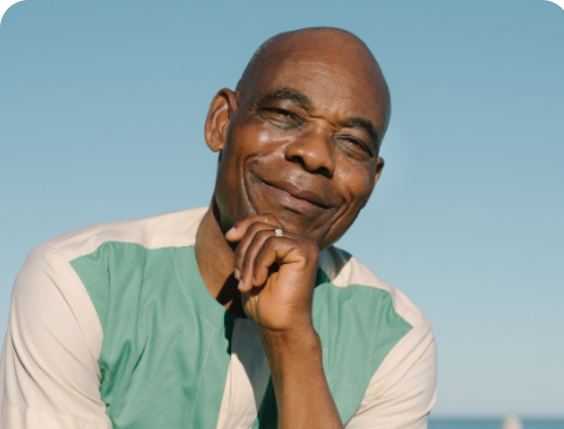 A smiling person resting their chin on their hand outdoors against a clear blue sky.