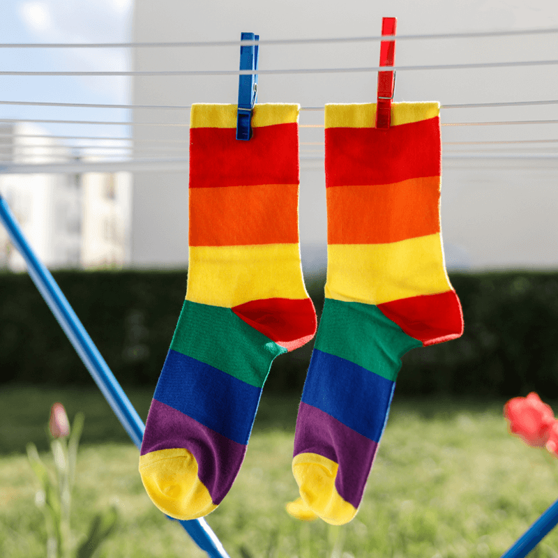 Two pairs of rainbow-striped socks hanging from a clothesline with pegs outdoors.