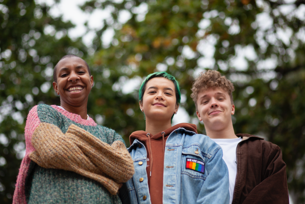 Three young people standing outdoors together, smiling confidently at the camera.