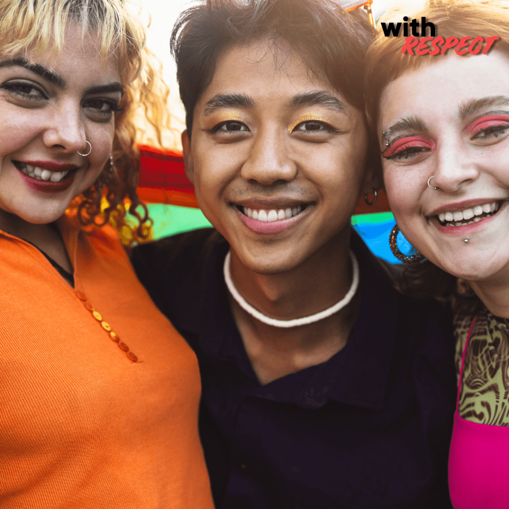 Three smiling people standing close together in front of a rainbow Pride flag.